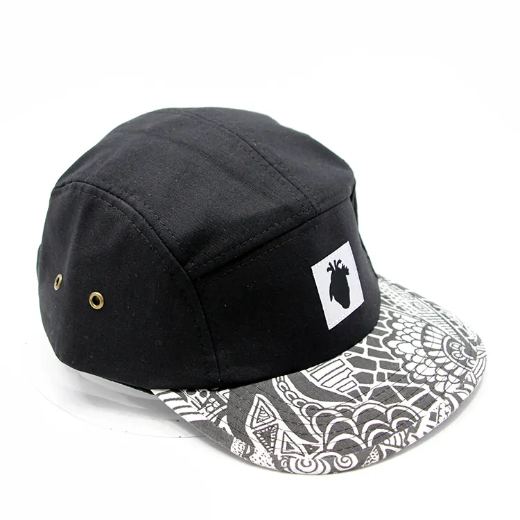 Three-quarter view of a black camp cap with a white square front badge and black-and-white patterned brim.