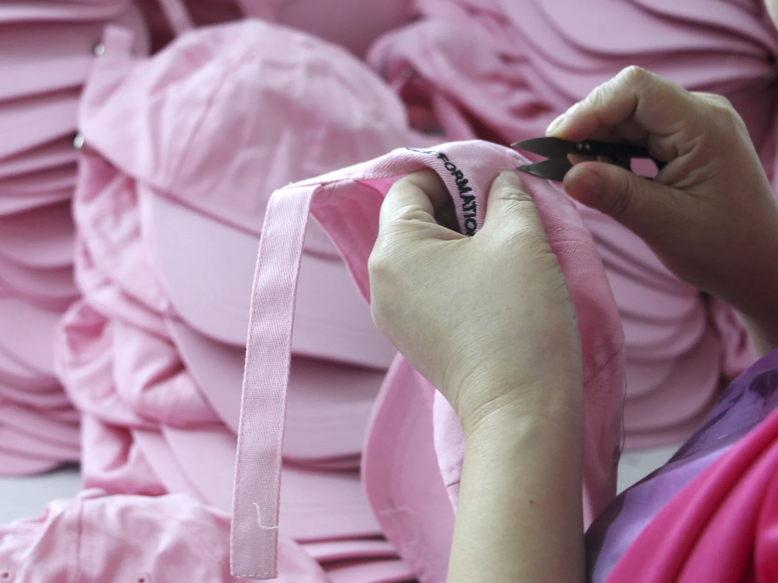 Close-up of loose threads being trimmed from a pink cap adjustment strap.