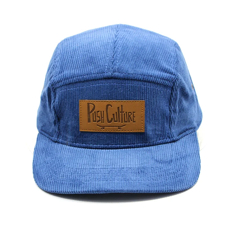 Front view of a blue corduroy camp cap with a brown rectangular patch and a flat brim.