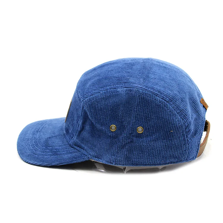 Side view of the blue corduroy camp cap showing two metal eyelets and a brown adjustment strap.