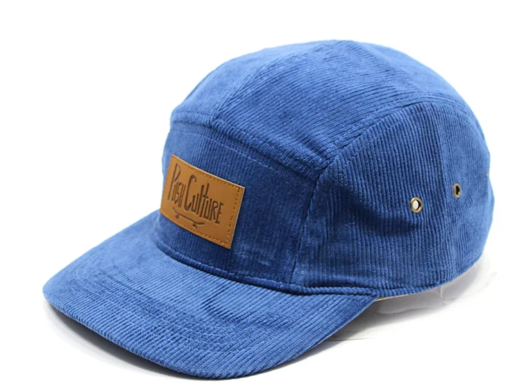 Blue corduroy camp cap with a brown rectangular front patch and metal eyelets.