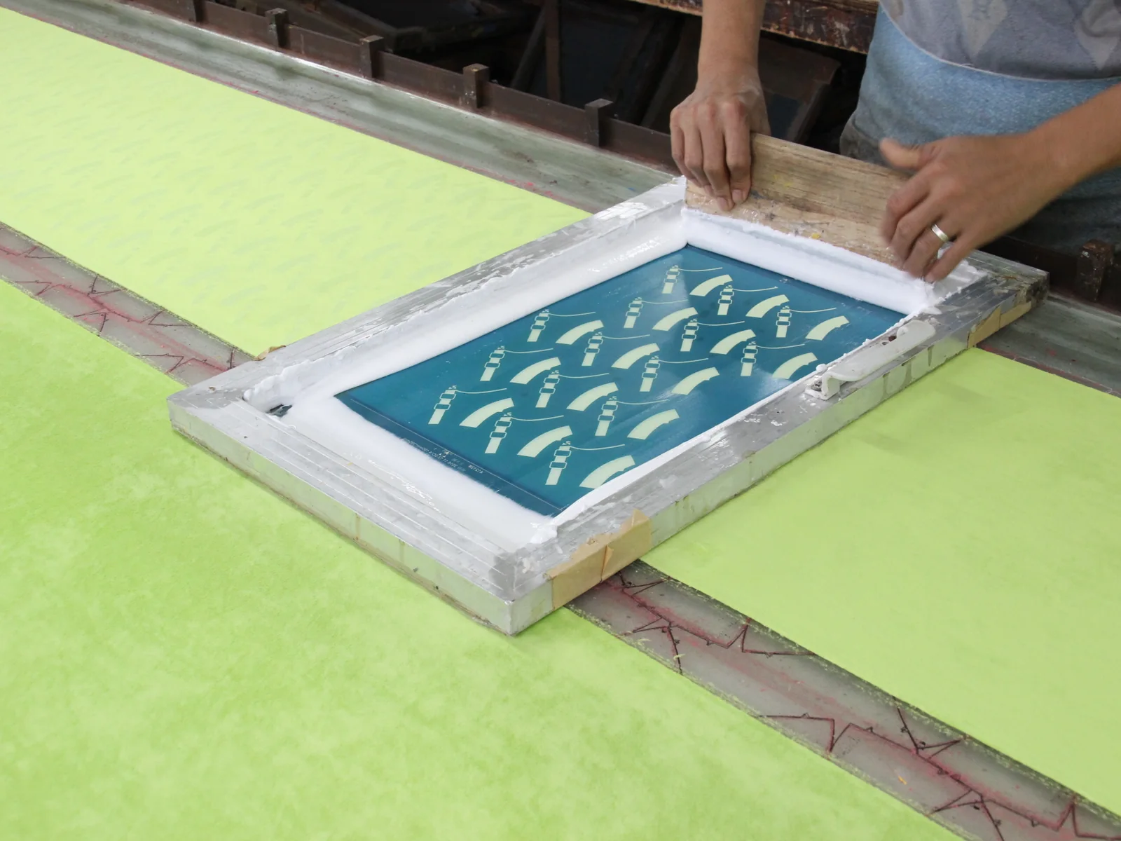 Hands using a squeegee on a screen-printing frame over fabric.
